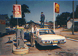 Bud standing on roof of car at filling station